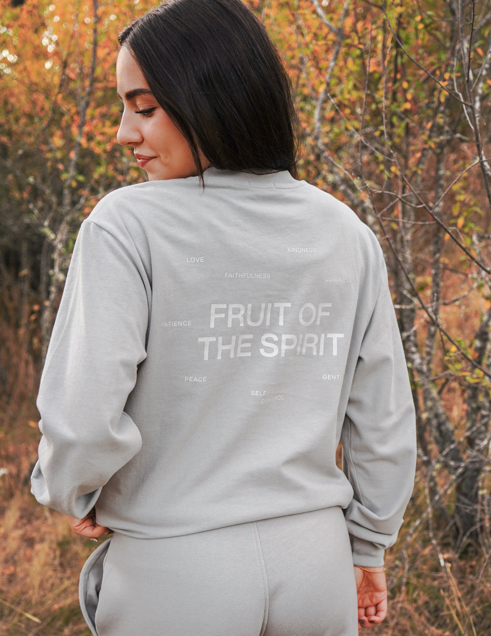 Woman wearing a gray sweatshirt with 'Fruit of the Spirit' text in an autumn setting