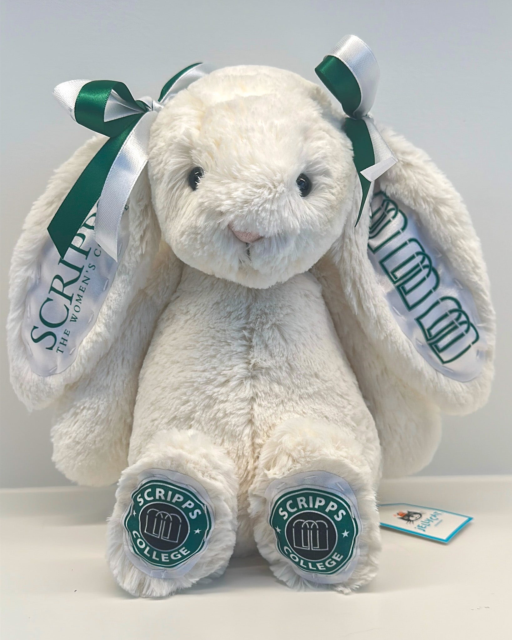 White plush bunny with green ribbons and 'Scripps College' branding on a white background