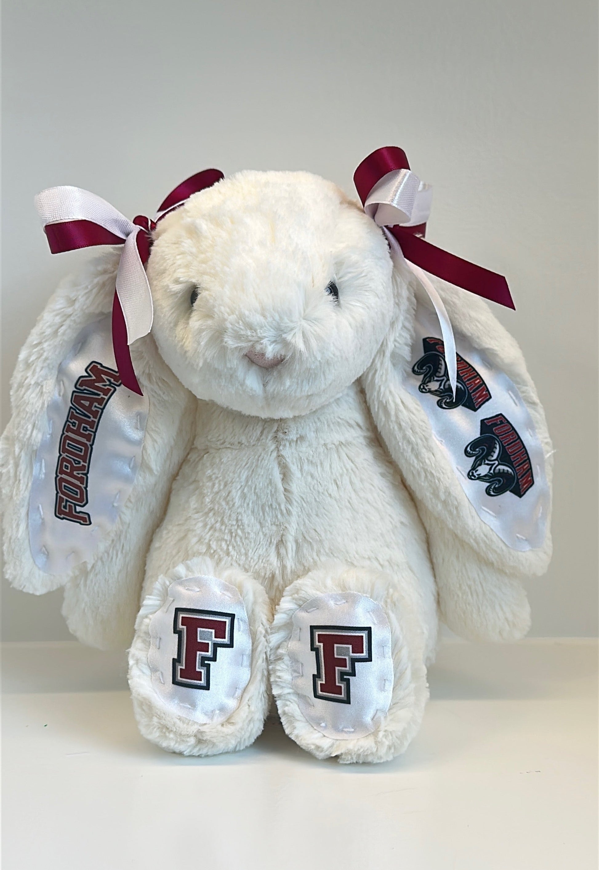 White stuffed bunny with red bows and 'F' logos on a white background