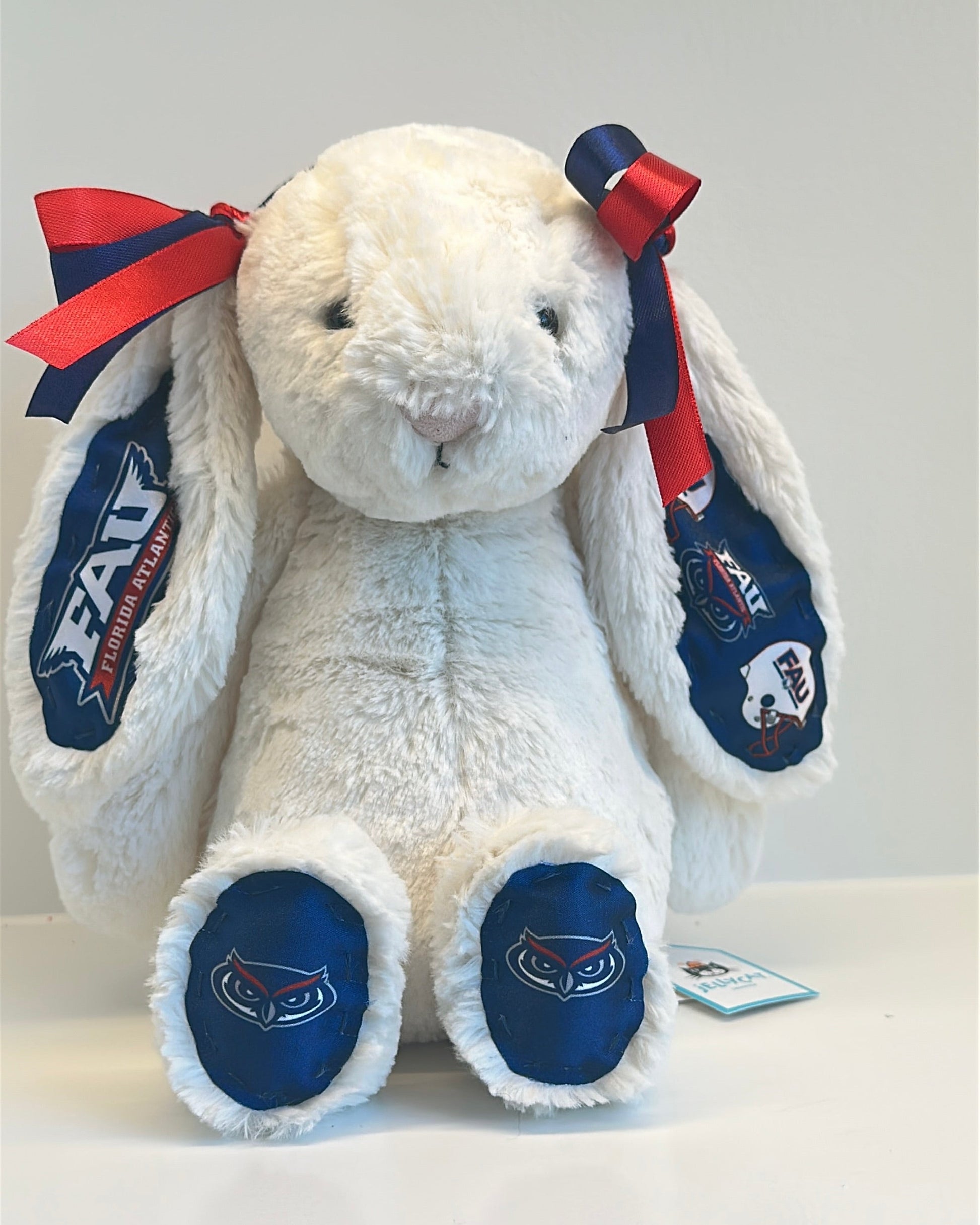 White plush bunny with red and blue bows and 'EAU' branding on a gray background