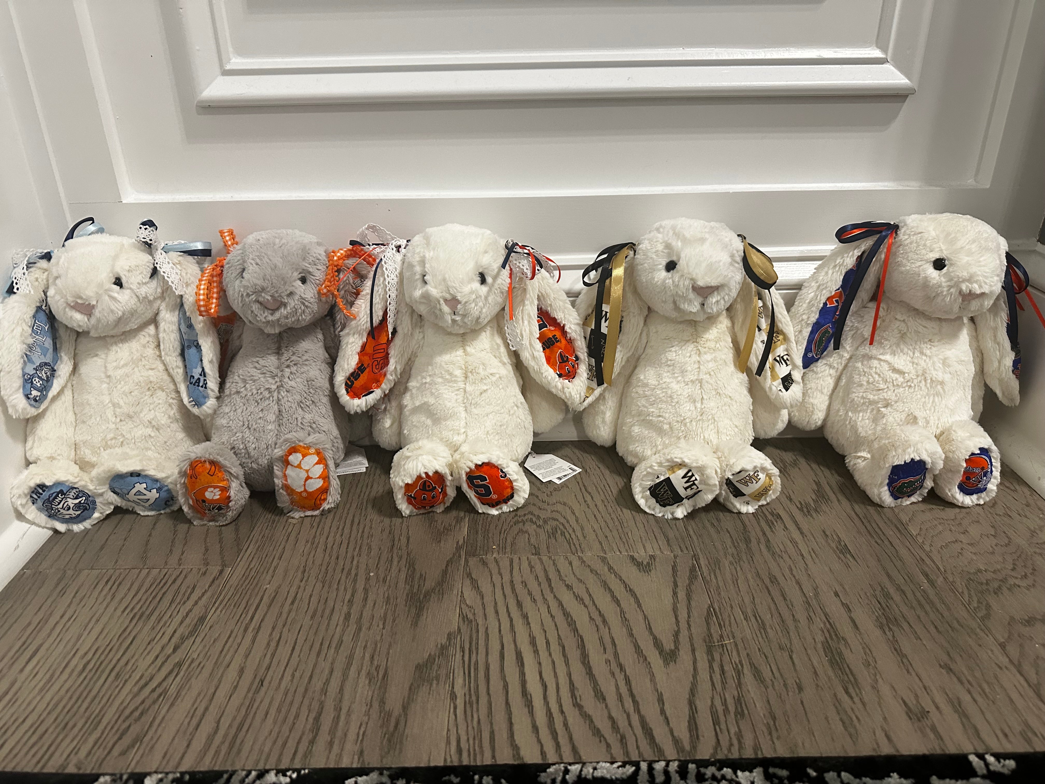 Five plush toys resembling bunnies with colorful accents on a wooden floor.