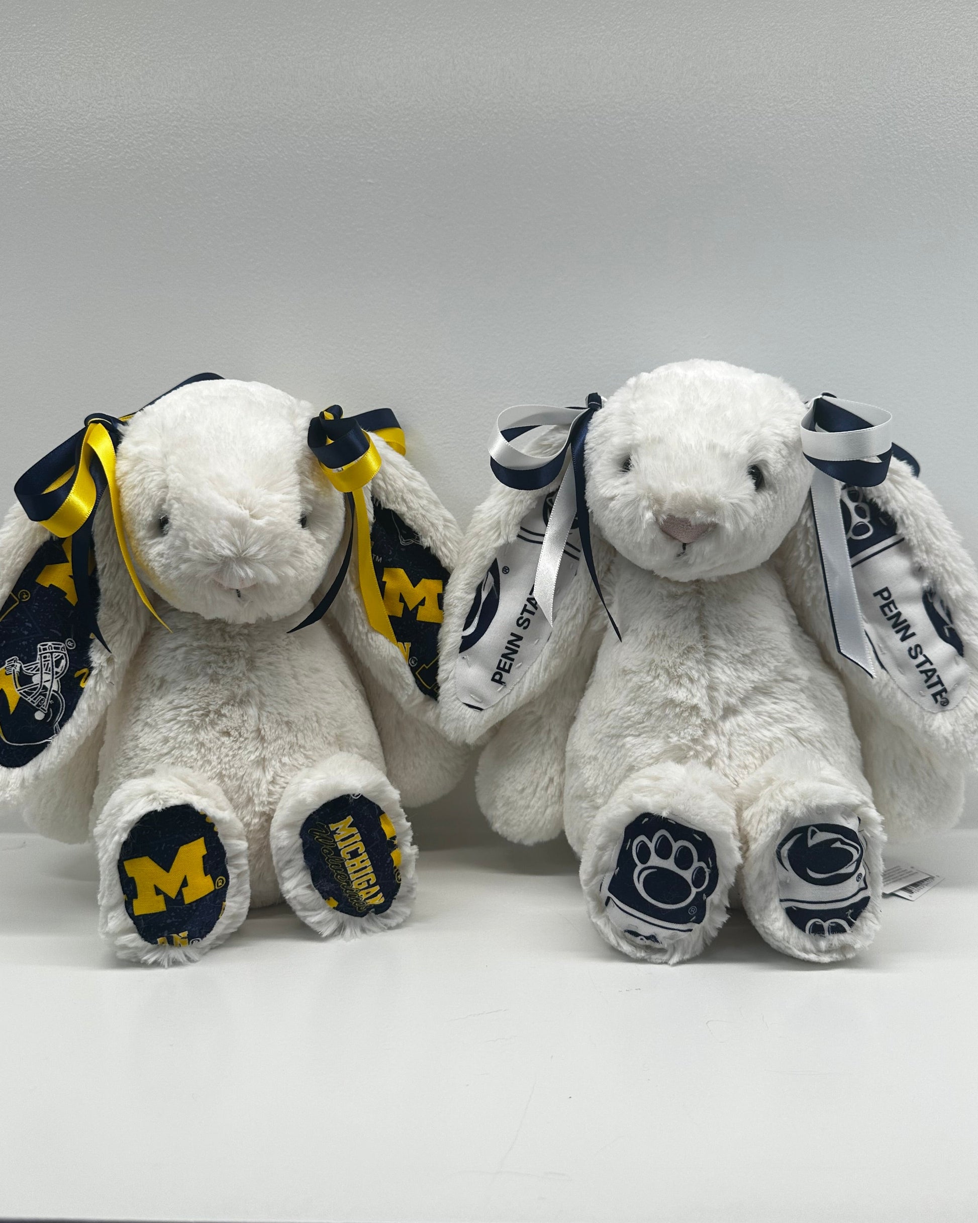 Two white stuffed animals with Michigan and Penn State logos on a white background