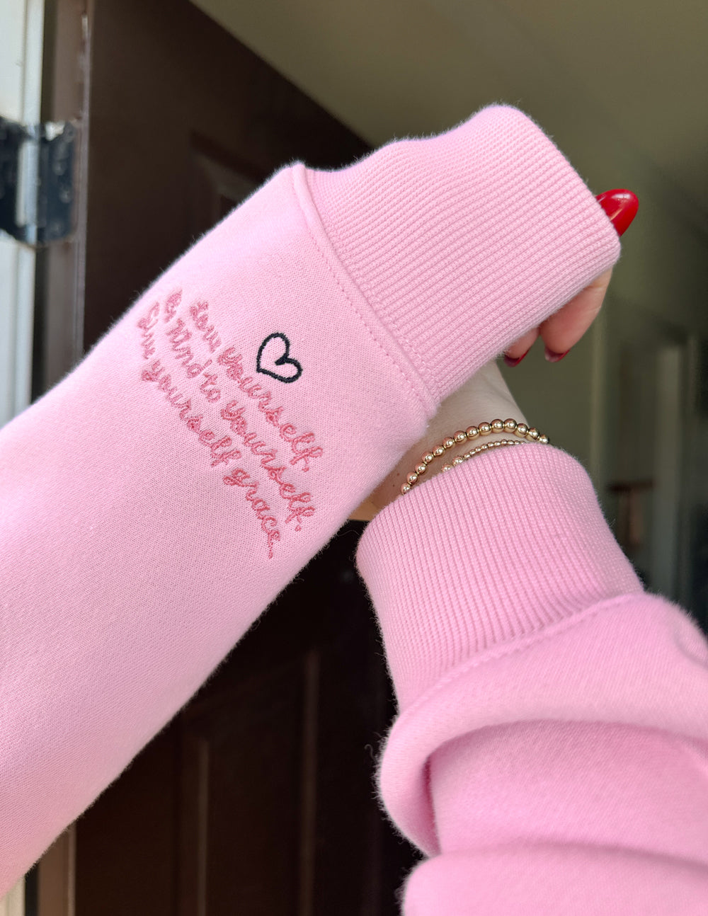 Pink sweatshirt with text and heart design held by a person.
