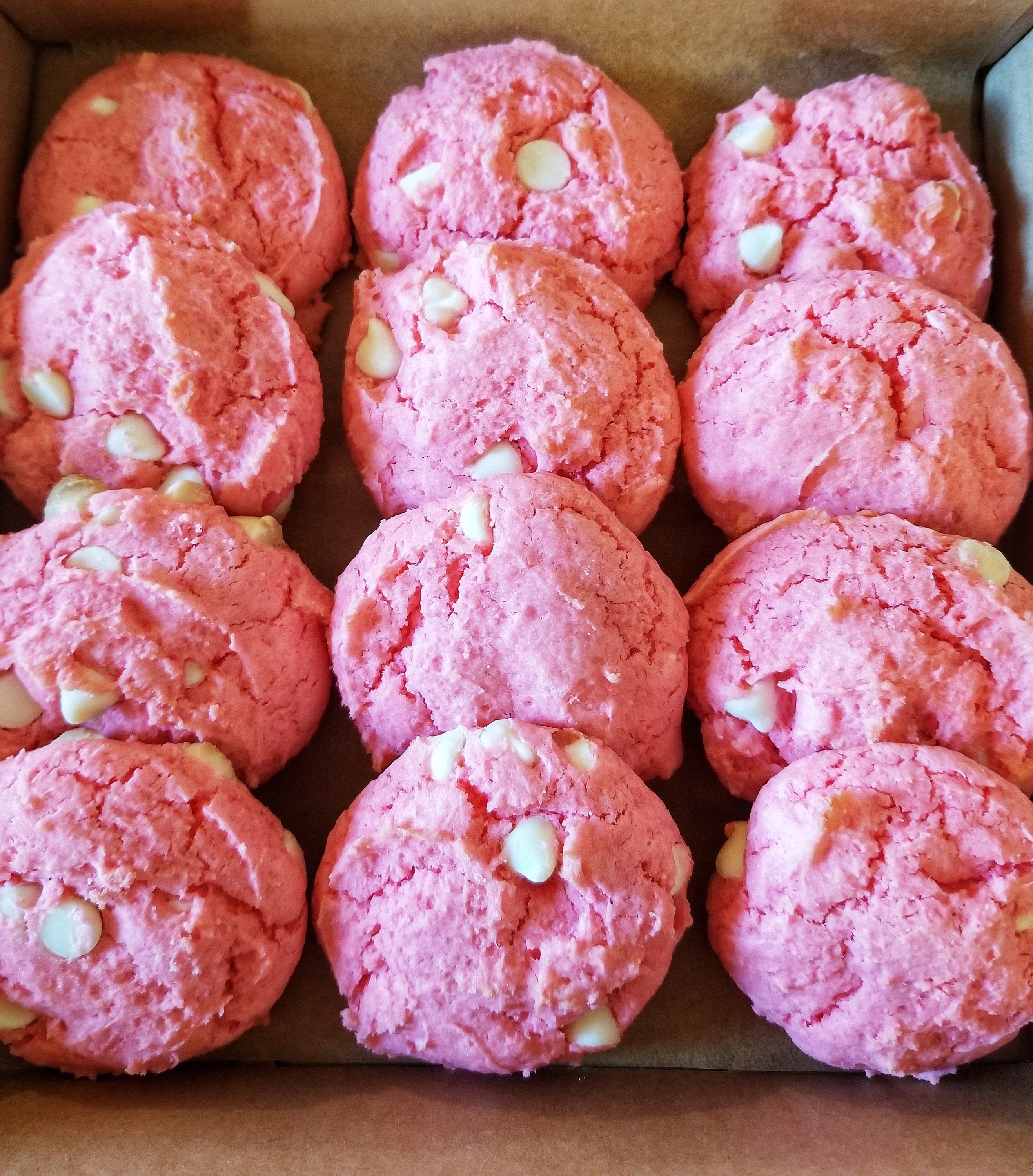 Box of pink cookies with white chips on a brown cardboard background