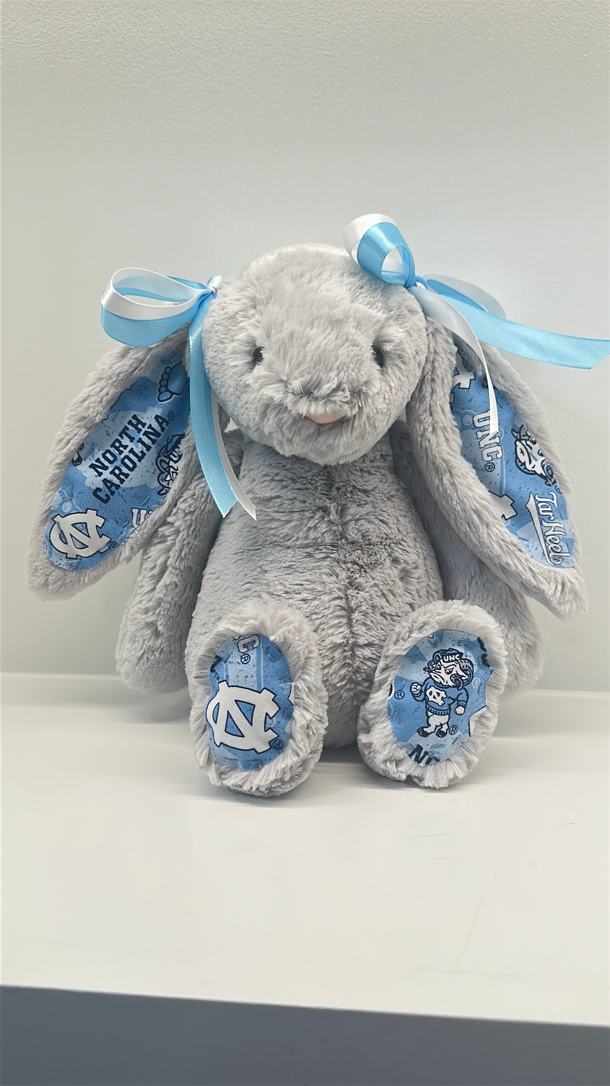 Gray plush bunny with blue ribbons and North Carolina logo on a white background