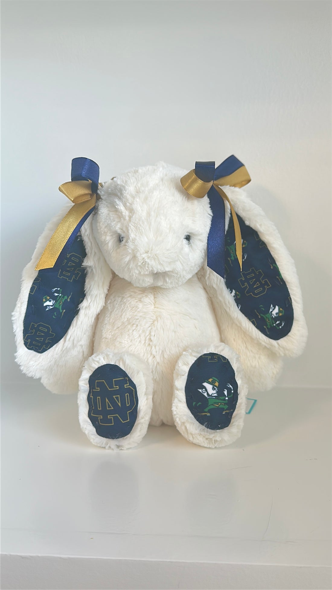 White plush bunny with blue paws and gold accents on a white background university notre dame logo
