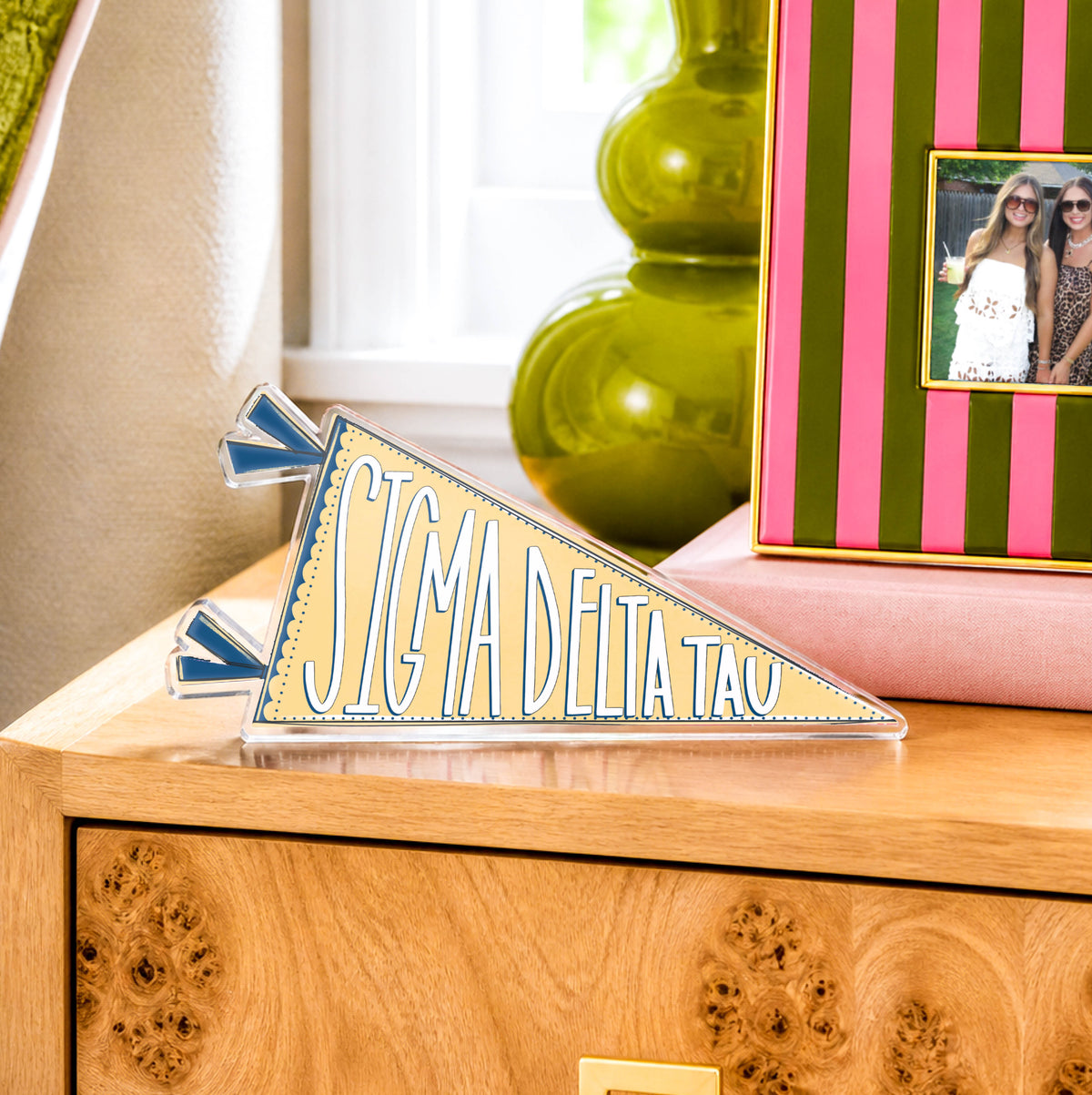 Sigma Delta Tau pennant on a wooden surface with a striped photo frame in the background