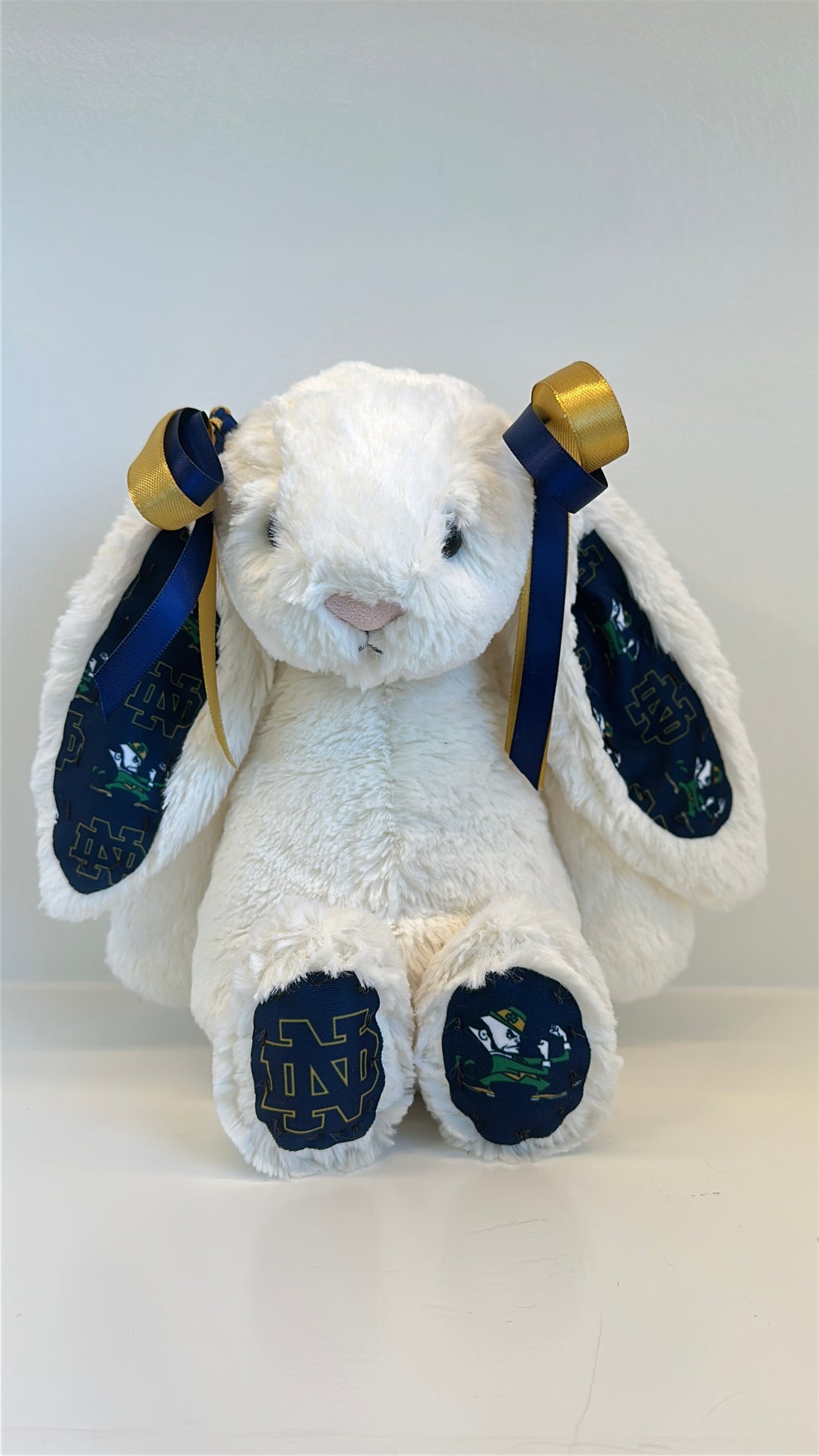 White plush bunny with blue paws and gold accents on a white background university notre dame logo