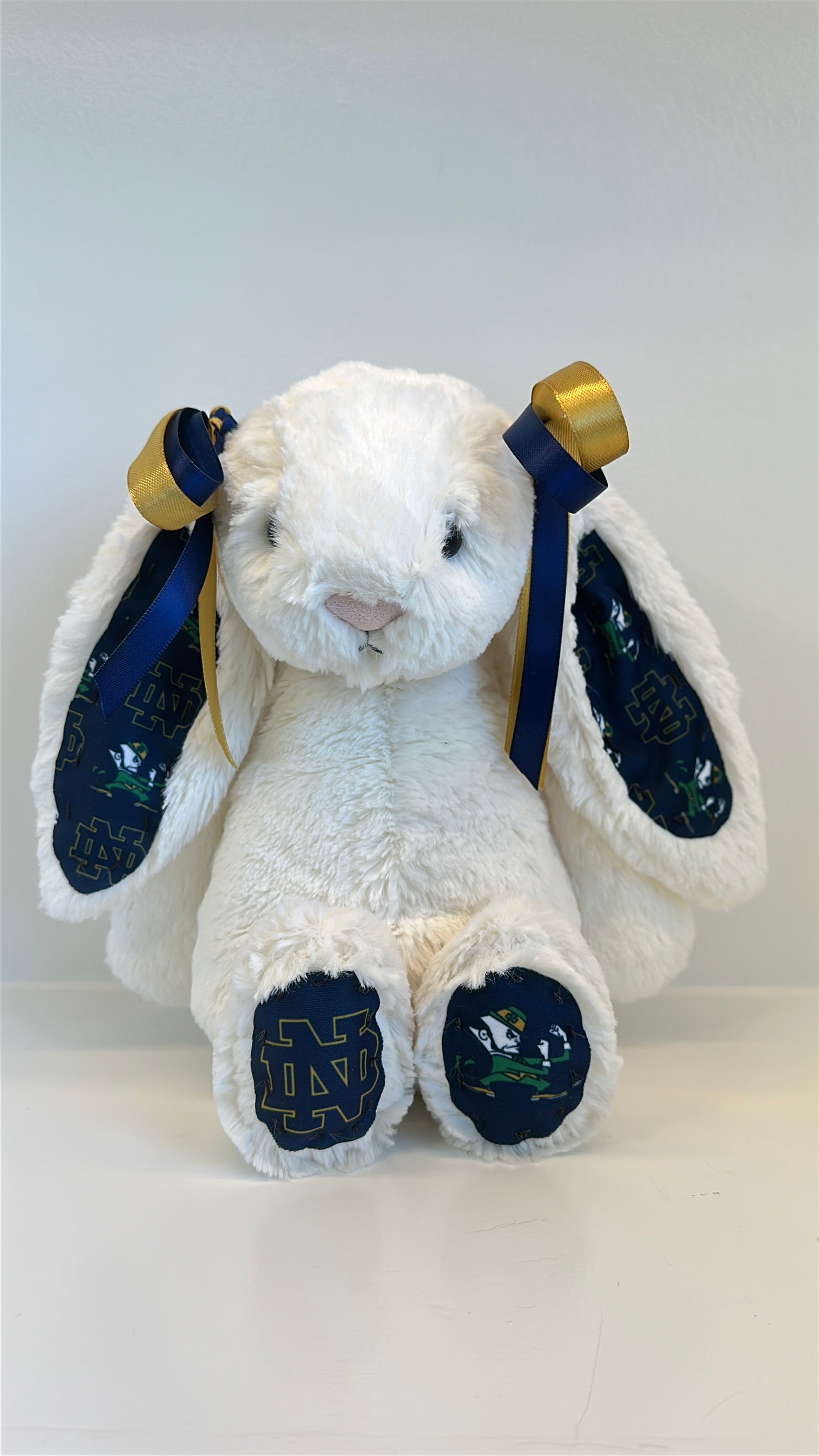 White plush bunny with blue paws and gold accents on a white background university notre dame logo